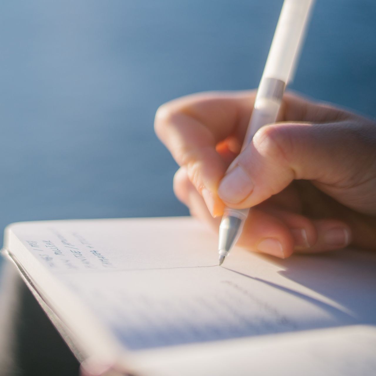 Main tenant un stylo blanc au-dessus d'un cahier à lignes sur fond bleu