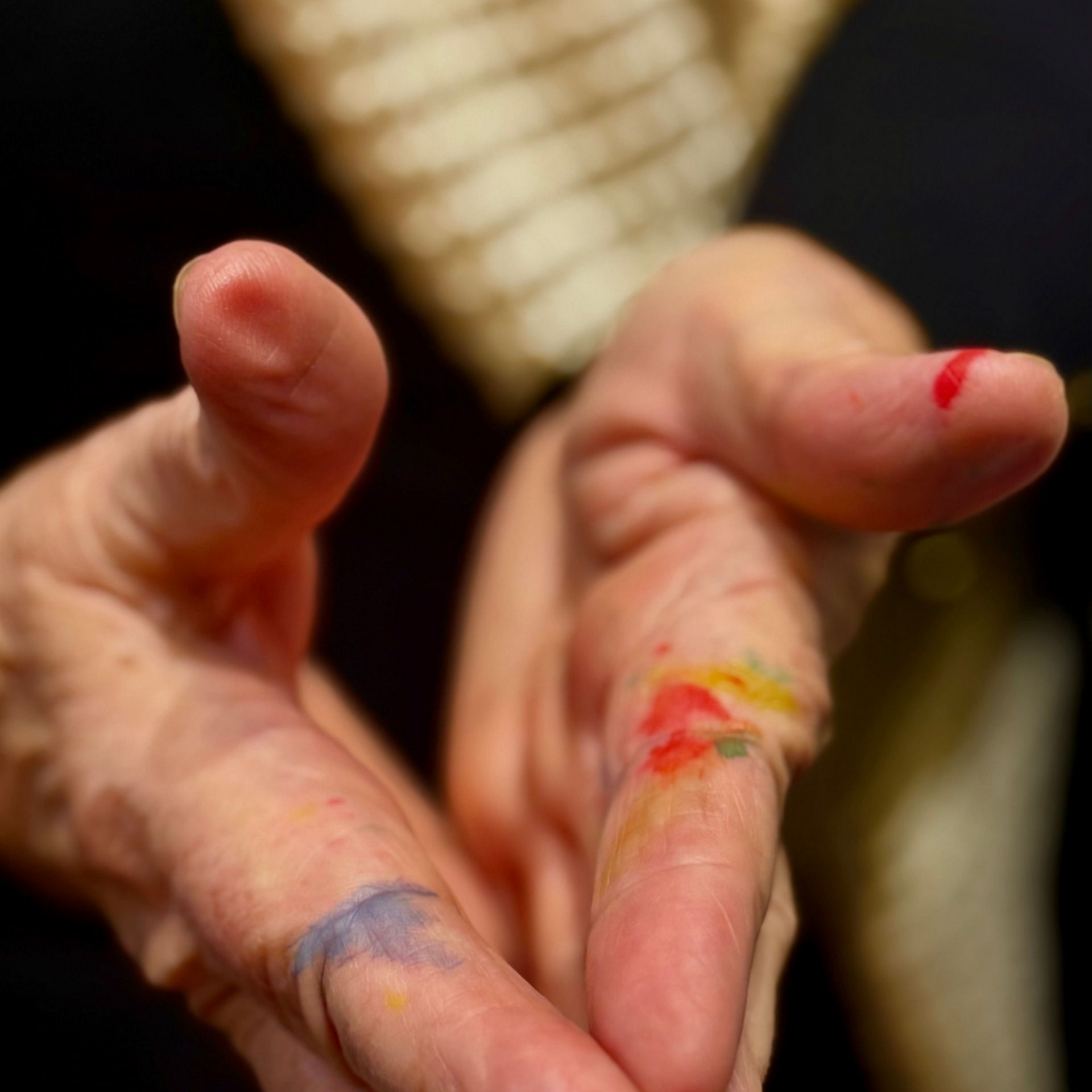 Des mains maculées de peinture, tendues vers l'avant, avec de la peinture colorée sur les doigts et les articulations.