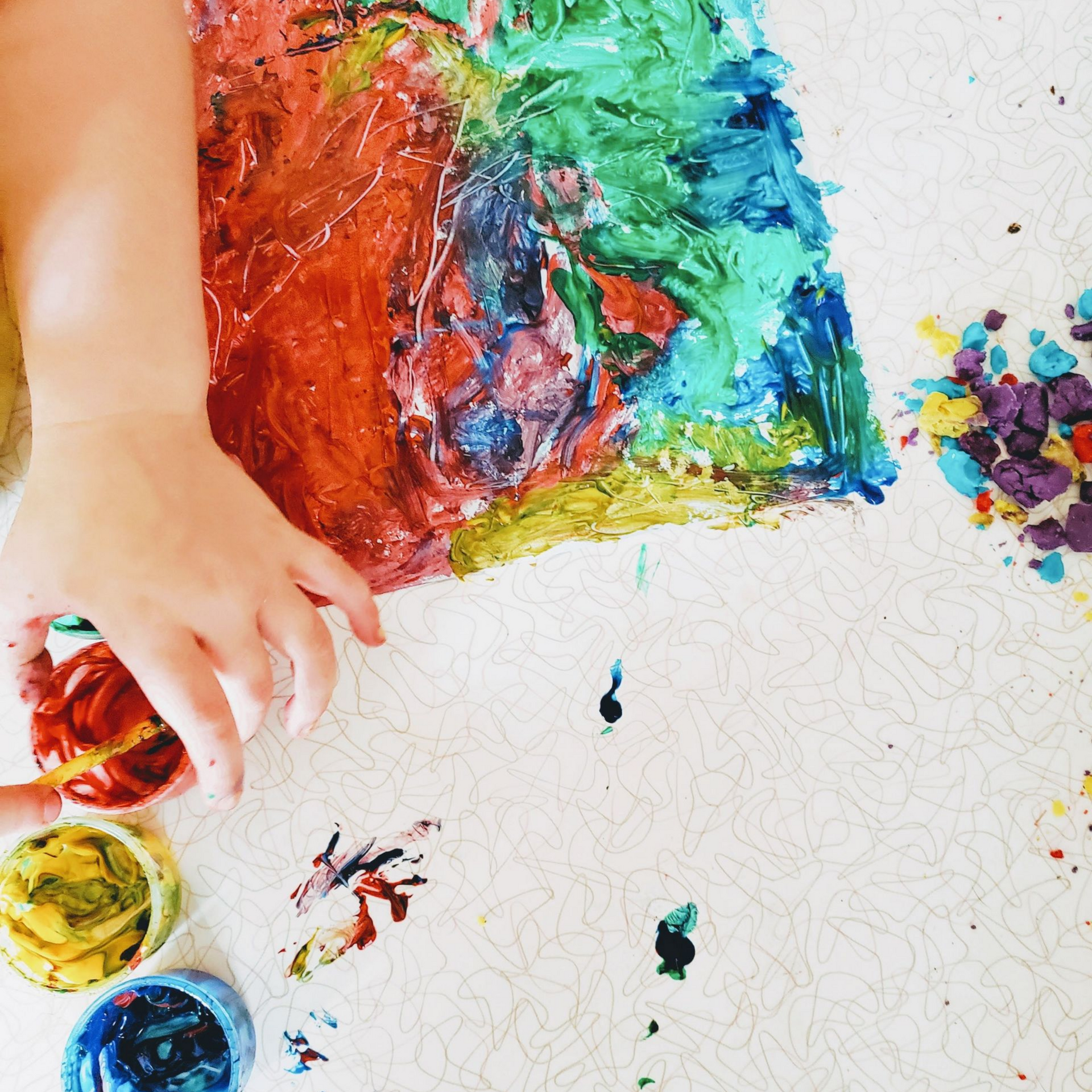 Main d'enfant peignant une toile abstraite colorée avec des pots de peinture sur une surface blanche