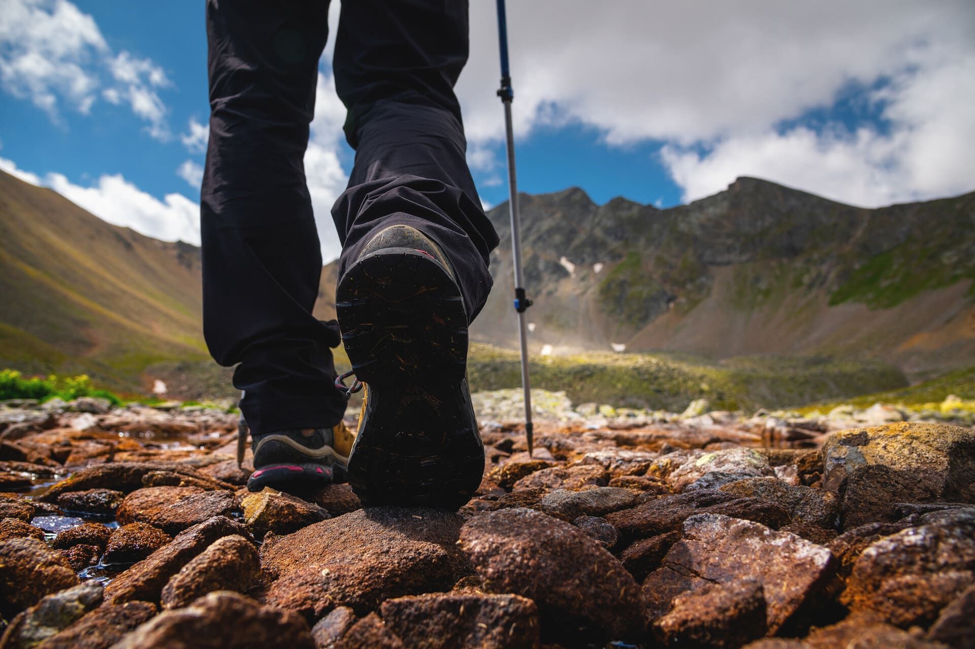 Hiking boots stepping on rocky terrain with mountains in the background.