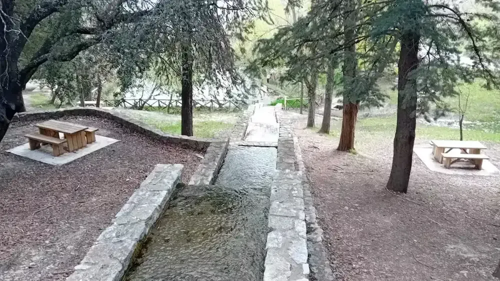 Canal de agua de piedra a través de un parque con mesas de picnic y árboles.