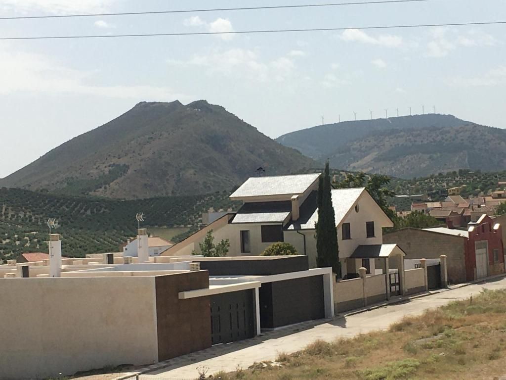 Casas con tejados gris oscuro frente a una sierra con olivos, bajo un cielo luminoso y soleado.