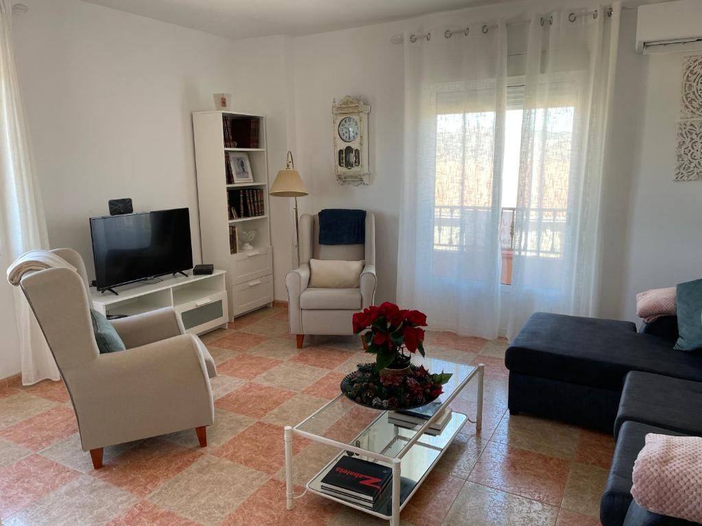 Sala de estar con paredes blancas, piso de baldosas, muebles y una ventana con cortinas transparentes.