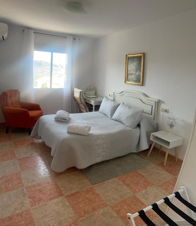 Dormitorio con cama, silla naranja, obras de arte y suelo de baldosas a cuadros.