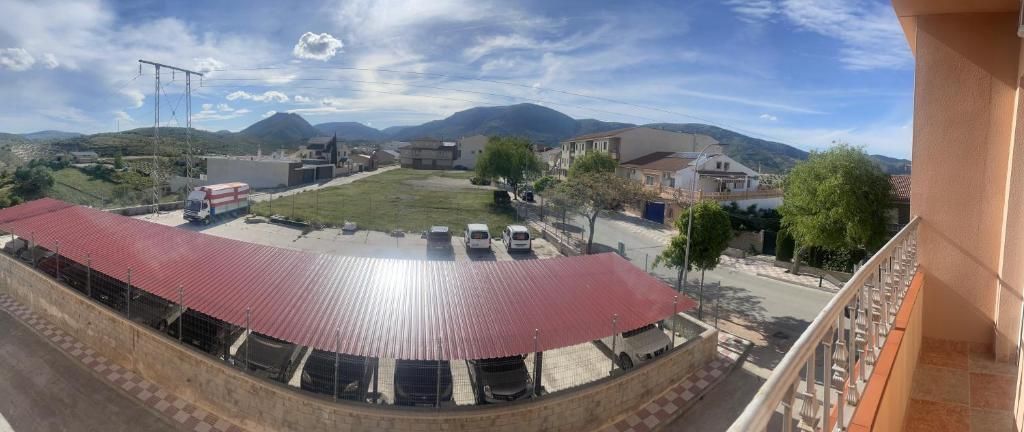 Vista desde un balcón a una calle, estacionamiento con plazas techadas y montañas a lo lejos.