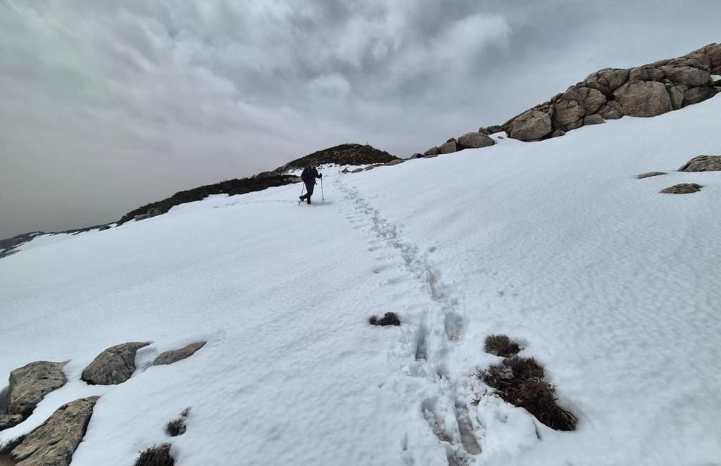 Persona caminando cuesta arriba a través de la nieve, siguiendo huellas, cielo nublado.