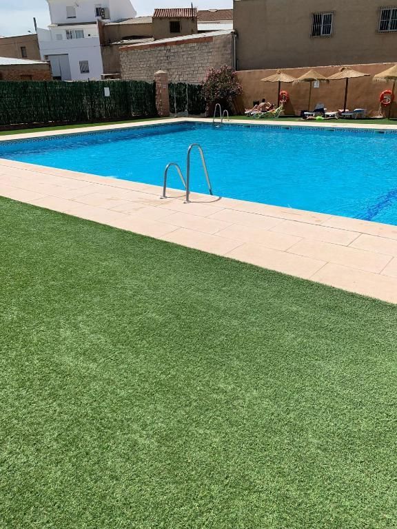 Piscina de agua azul rodeada de césped verde artificial y azulejos beige.