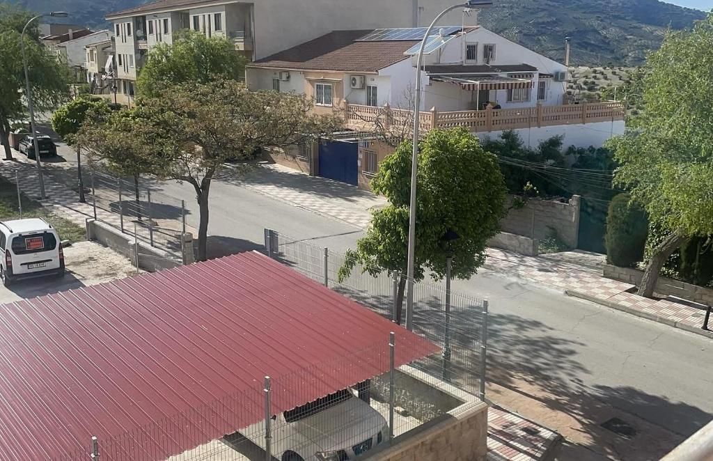 Vista de la calle: Autos estacionados a lo largo de una carretera con casas y árboles bajo un cielo soleado.