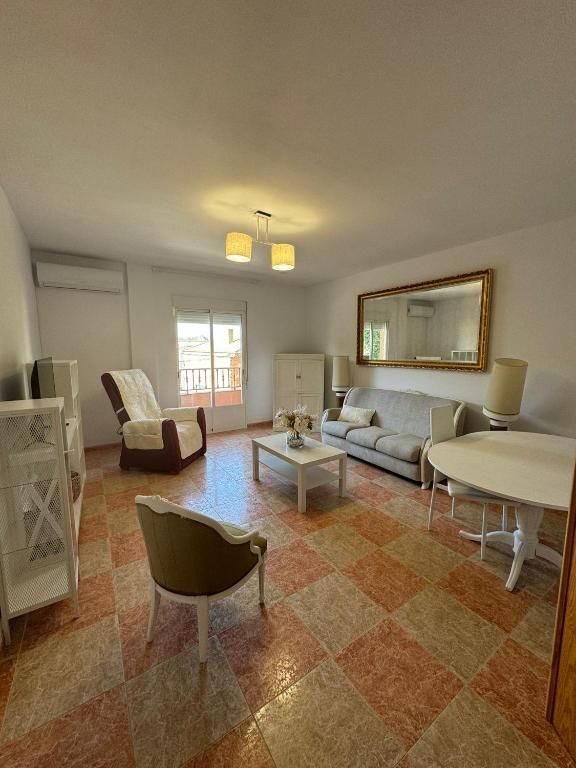 Sala de estar con suelo a cuadros blancos y naranjas, sofá, sillas, espejo y muebles blancos.