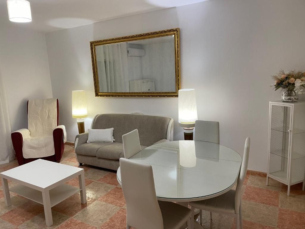 Sala de estar con sofá, sillas, mesa, espejo y armario. Luminosa, con paredes blancas y azulejos rojos.