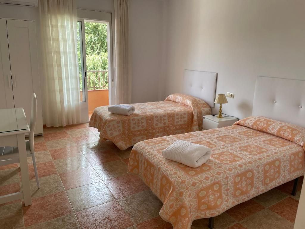 Dormitorio con dos camas individuales, colchas con estampados naranjas, cabeceros blancos y balcón.