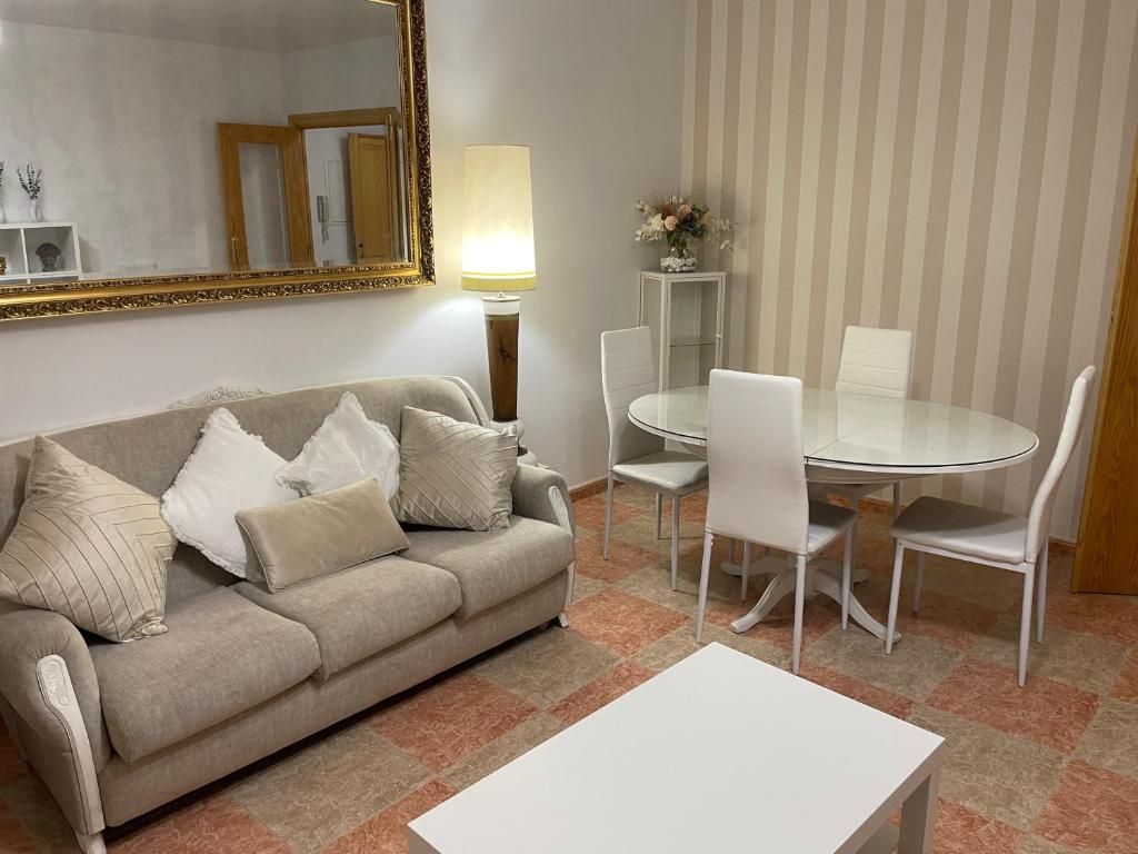 Vista de una calle de una ciudad con edificios, árboles y montañas en la distancia bajo un cielo azul.