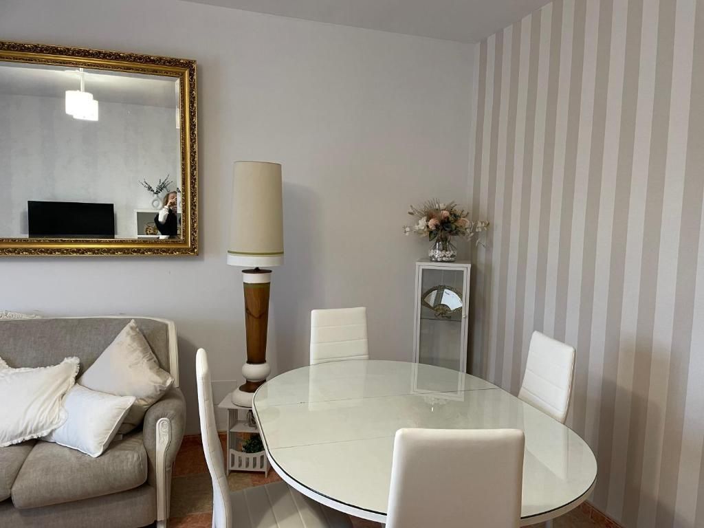 Comedor con mesa ovalada, sillas blancas, lámpara alta y espejo con marco dorado. Papel pintado a rayas.