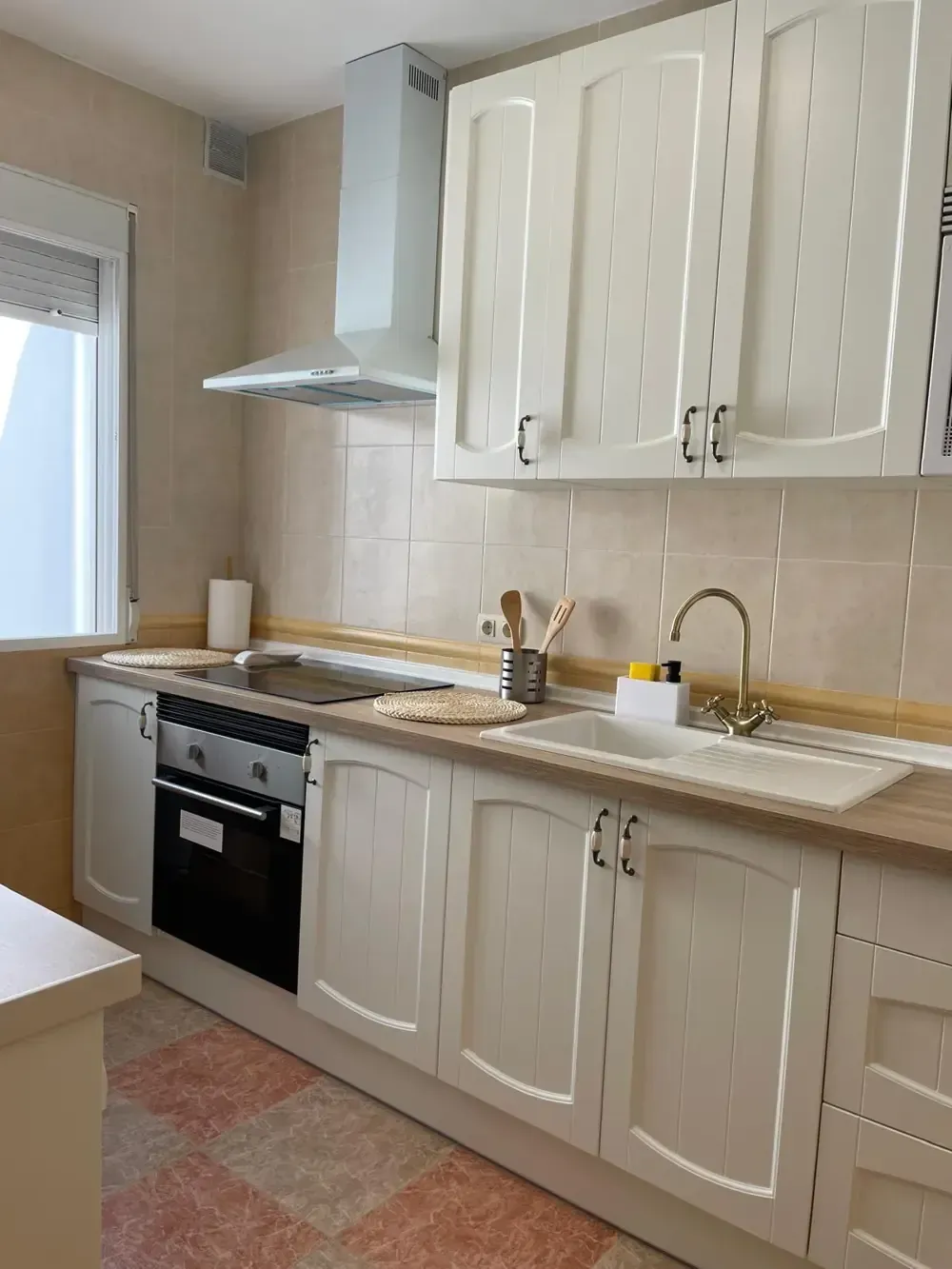 Gabinetes de cocina blancos con electrodomésticos y fregadero contra un protector contra salpicaduras de azulejos beige.