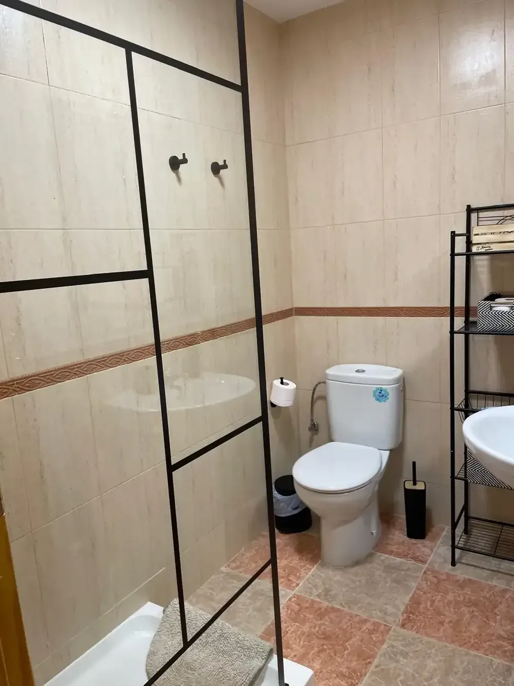 Baño con azulejos de color beige y marrón, mampara de ducha de cristal y un inodoro.