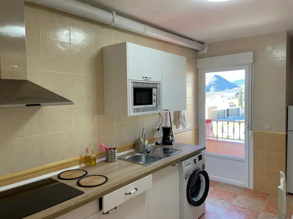 Cocina con encimeras de madera clara, armarios blancos y microondas. Hay una lavadora a la vista.