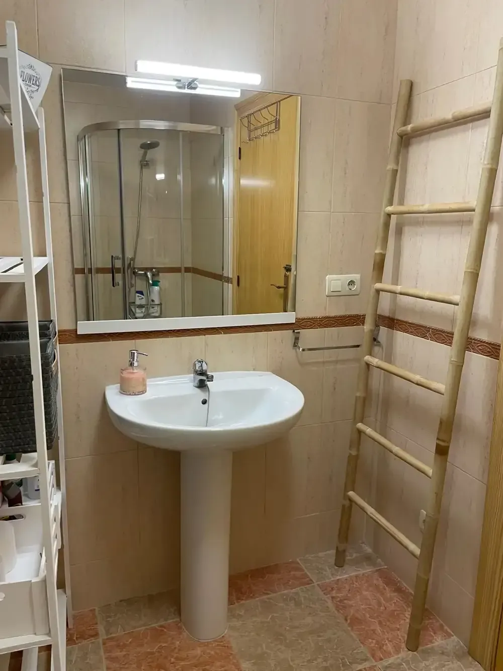 Baño con lavabo de pedestal, espejo, ducha y escalera de madera para toallas.