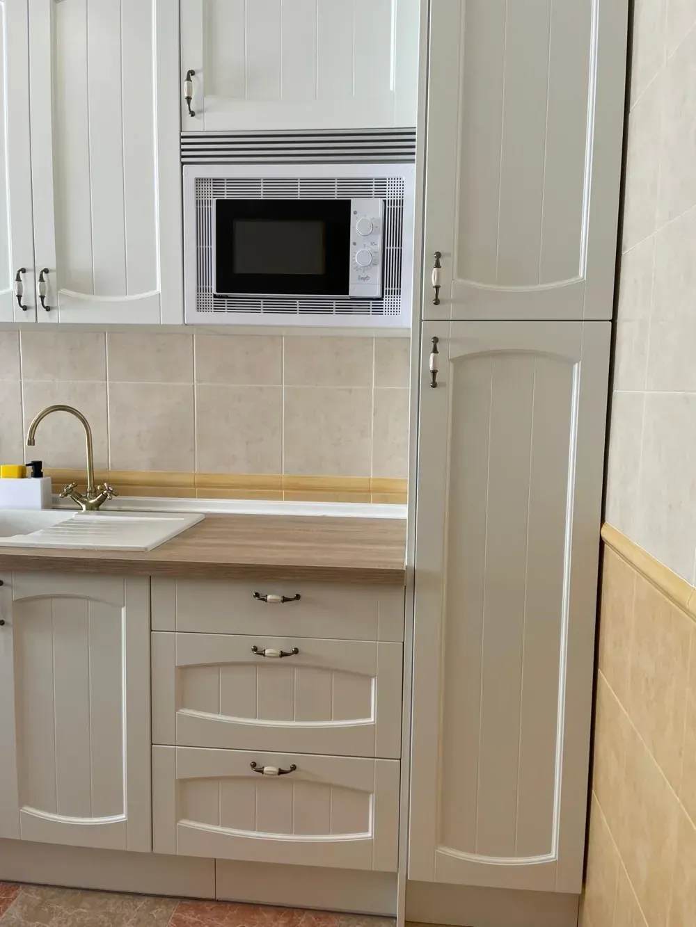 Gabinetes de cocina blancos con microondas incorporado sobre un fregadero y una encimera.