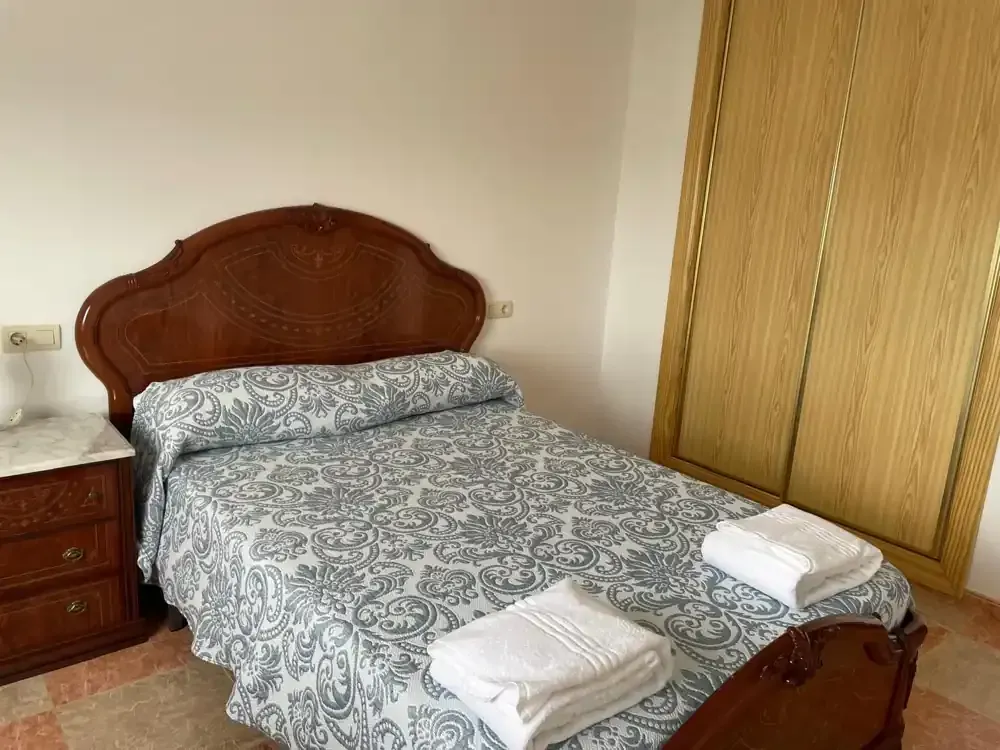 Dormitorio con cama, mesita de noche y armario. La cama tiene ropa de cama con estampado floral y dos toallas blancas.