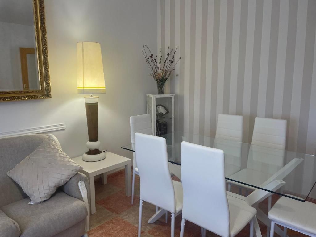 Comedor con mesa de cristal, sillas blancas y lámpara alta.