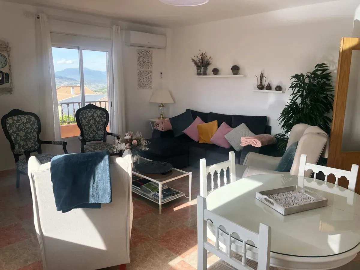 Conjunto de patio de hierro forjado blanco con mesa de mosaico y cojines estampados sobre una terraza de baldosas.