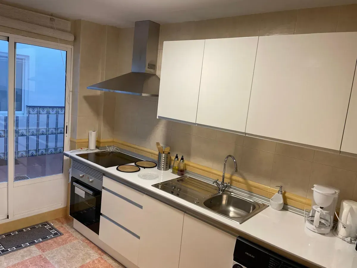 Cocina blanca con electrodomésticos y gabinetes de acero inoxidable, puerta corrediza a un balcón.