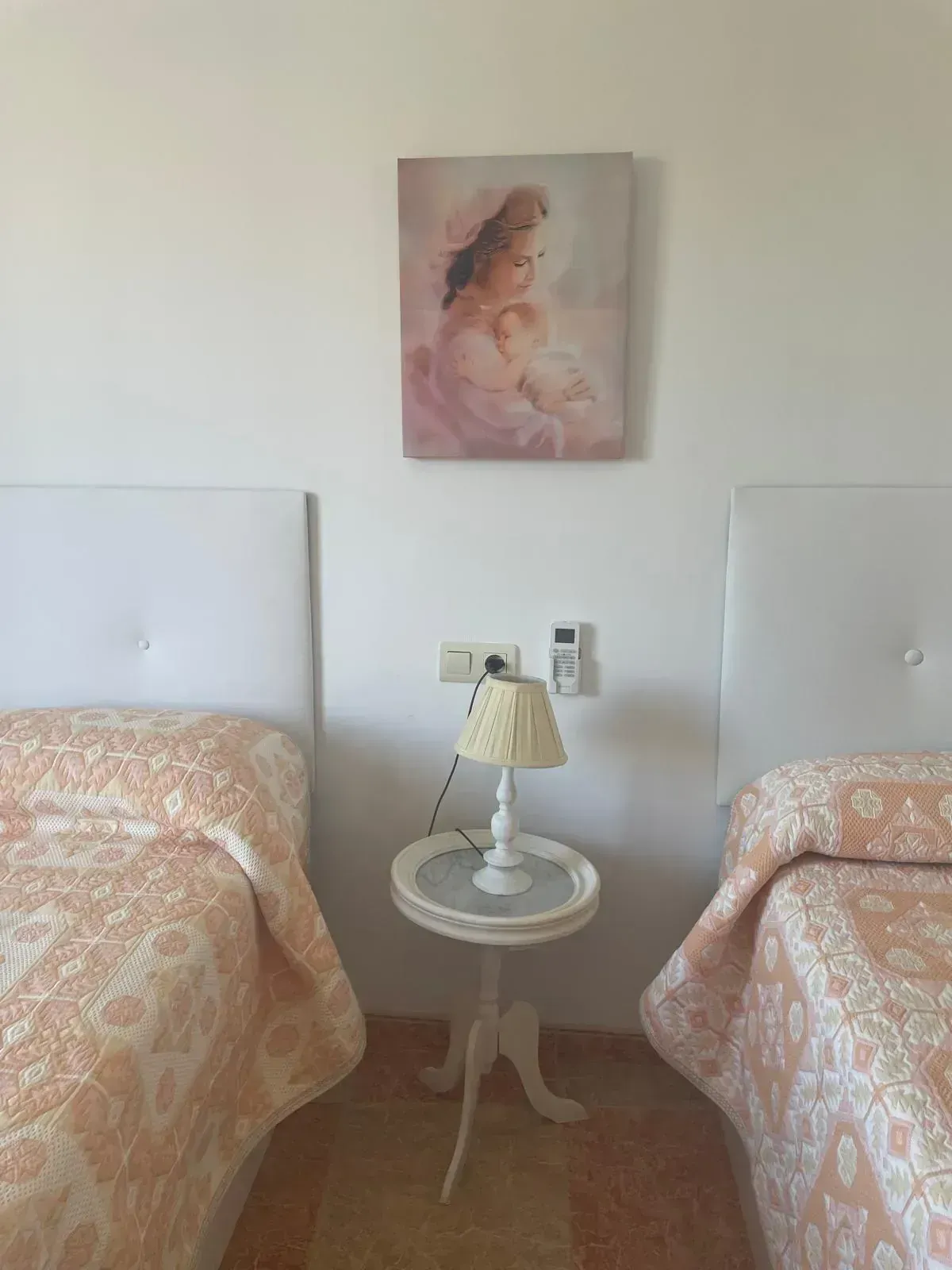 Dos camas con colchas color melocotón, una mesita con lámpara entre ellas y un cuadro en la pared.
