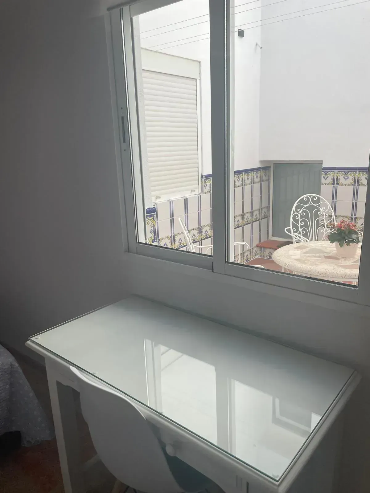 Escritorio blanco con silla junto a una ventana que da a un pequeño balcón con mesa y sillas.