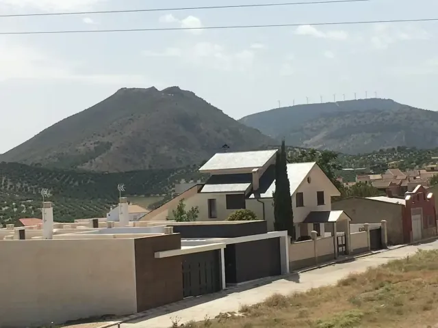 Casas y un camino frente a una cordillera bajo un cielo nublado.
