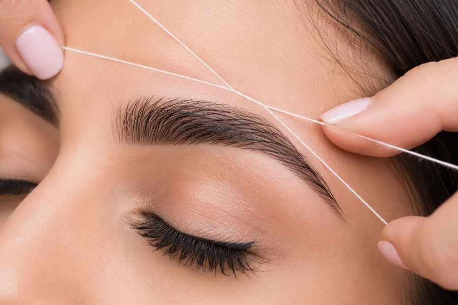 Depilación de cejas con hilo durante su sesión de aseo personal.