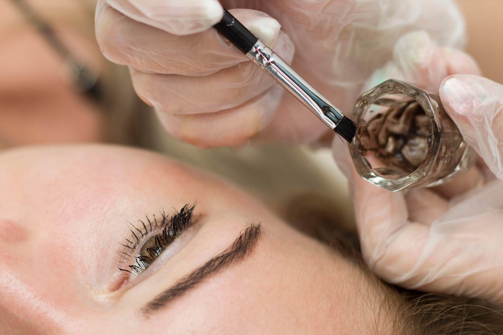 Esteticista aplicando tinte para cejas con un pincel durante un tratamiento de belleza.