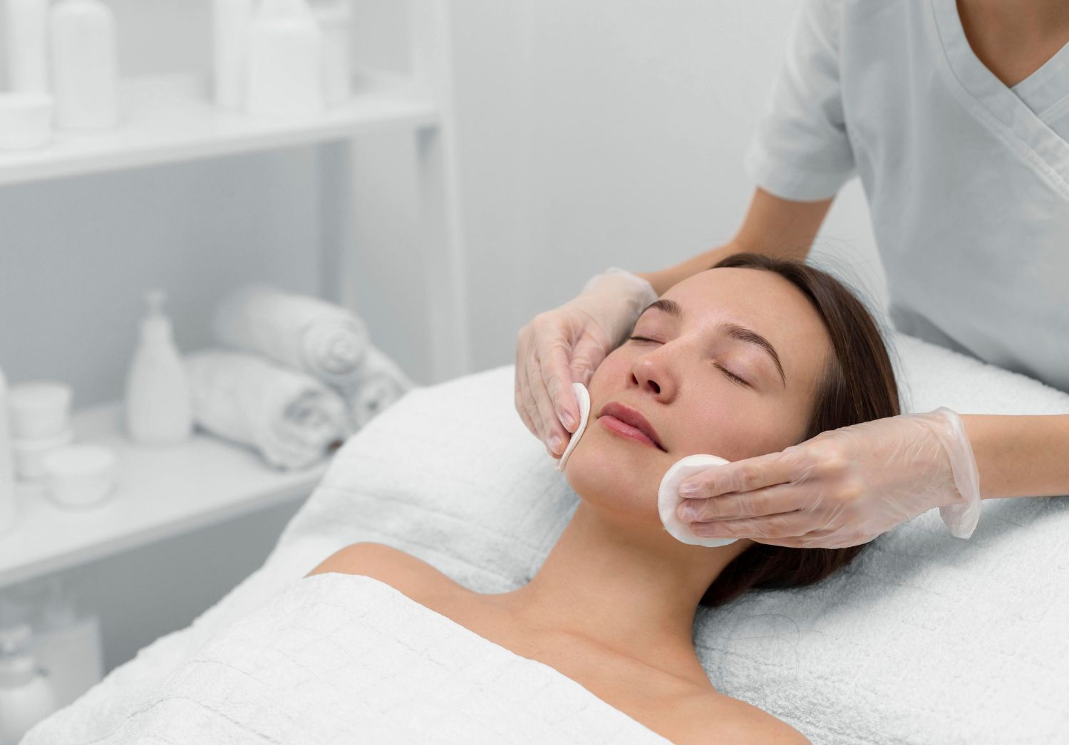 Tratamiento facial en un spa, con una clienta recibiendo un masaje facial con manos enguantadas.