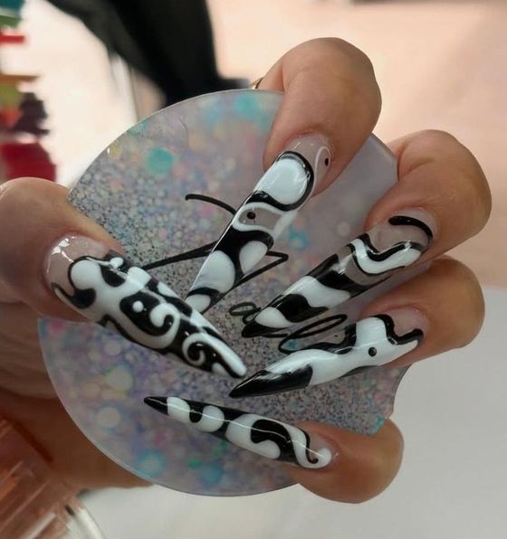 Mano con uñas decoradas con un diseño de espirales en blanco y negro, sosteniendo un abanico circular brillante.