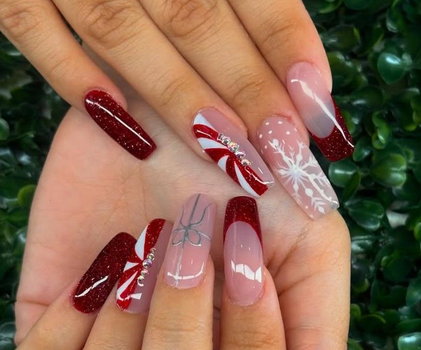Manos decoradas con diseños festivos en rojo, rosa y blanco, incluyendo copos de nieve y rayas de bastón de caramelo.
