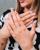 Primer plano de manos con largas uñas decoradas con flores cruzadas sobre una blusa estampada en blanco y negro.