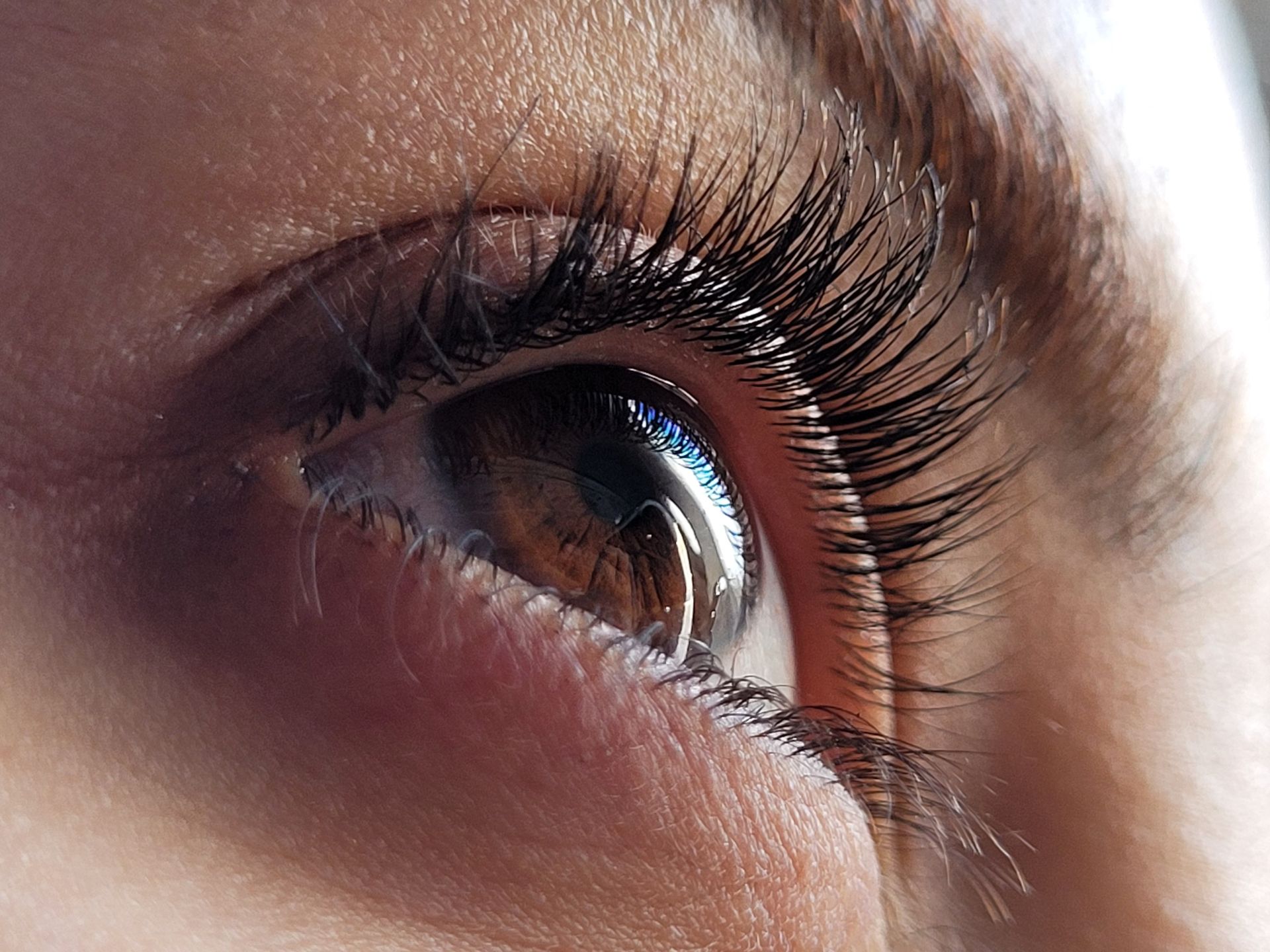 Primer plano de un ojo humano con pestañas largas y un reflejo en la pupila.