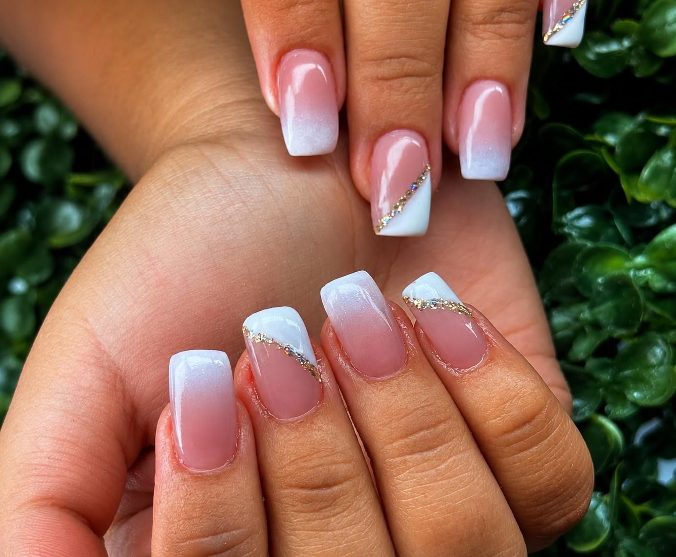 Manos con uñas pintadas con la técnica ombré rosa y detalles de purpurina plateada sobre un fondo verde.