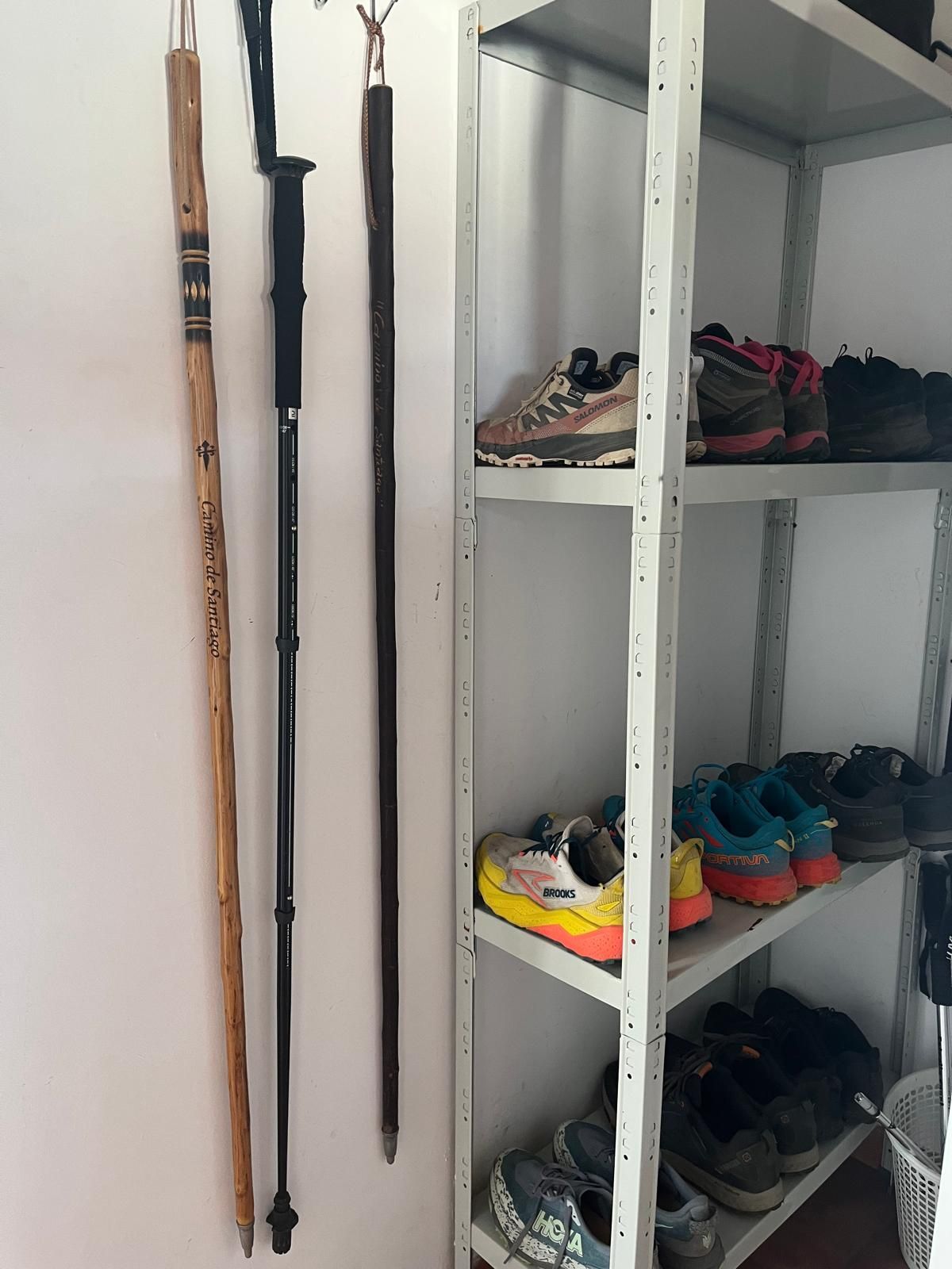 Tres bastones de senderismo están colgados en una pared junto a un zapatero.