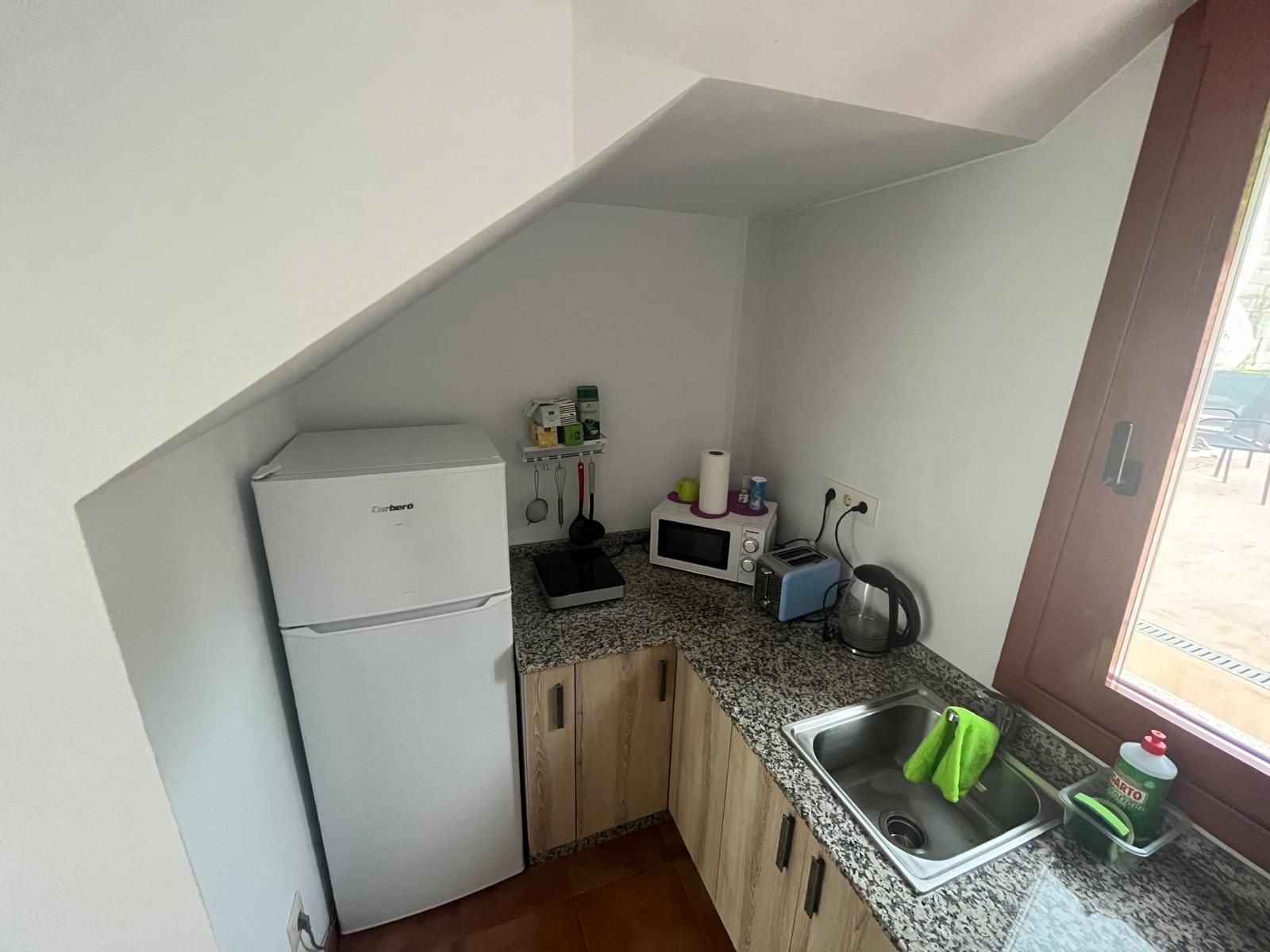 Una cocina con fregadero, frigorífico, microondas y ventana.