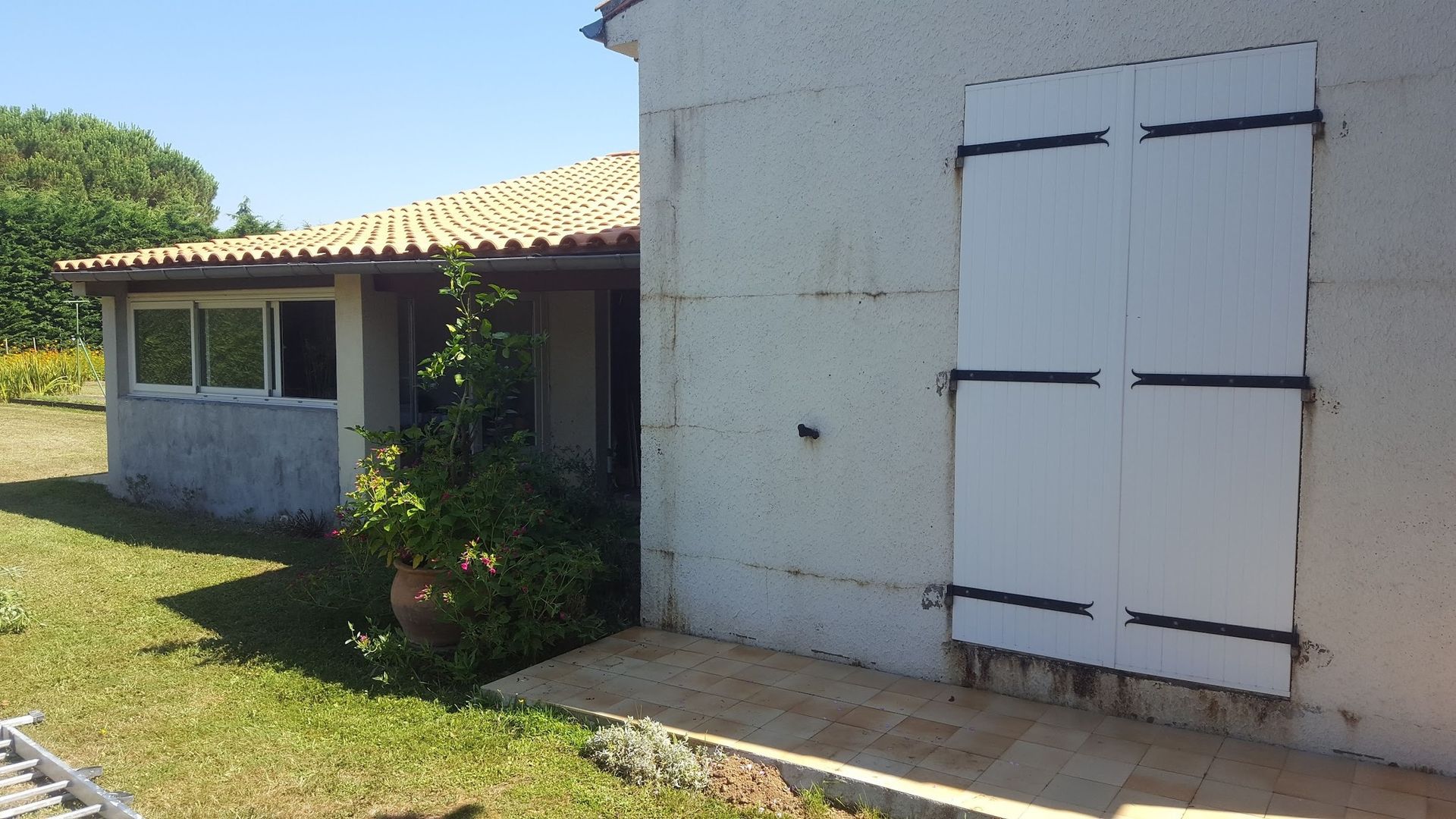 Vue latérale d'une maison blanche avec des volets blancs, une entrée couverte et de l'herbe verte.