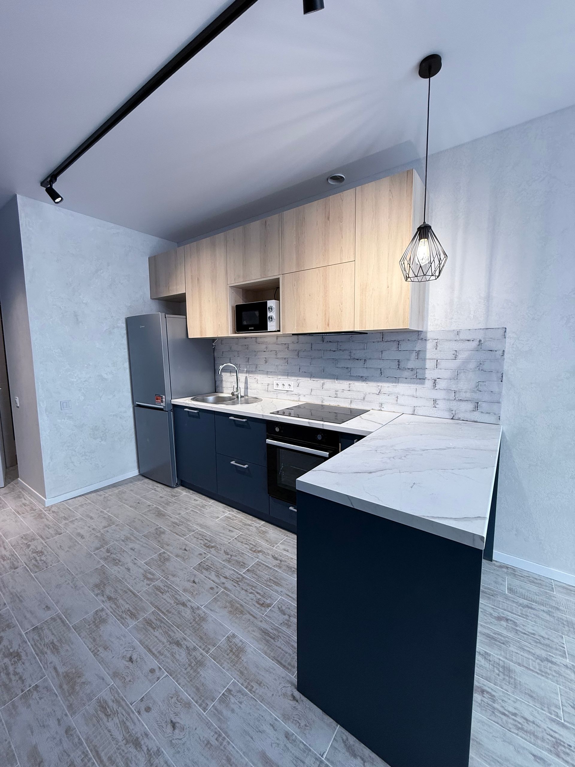 Cuisine moderne avec armoires bleu marine, dessus en bois clair, comptoir blanc, appareils électroménagers en acier inoxydable et suspension.