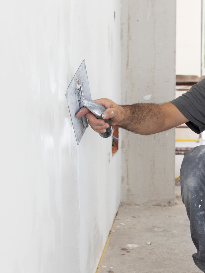 Personne utilisant une truelle pour appliquer du plâtre sur un mur blanc dans un contexte de construction.