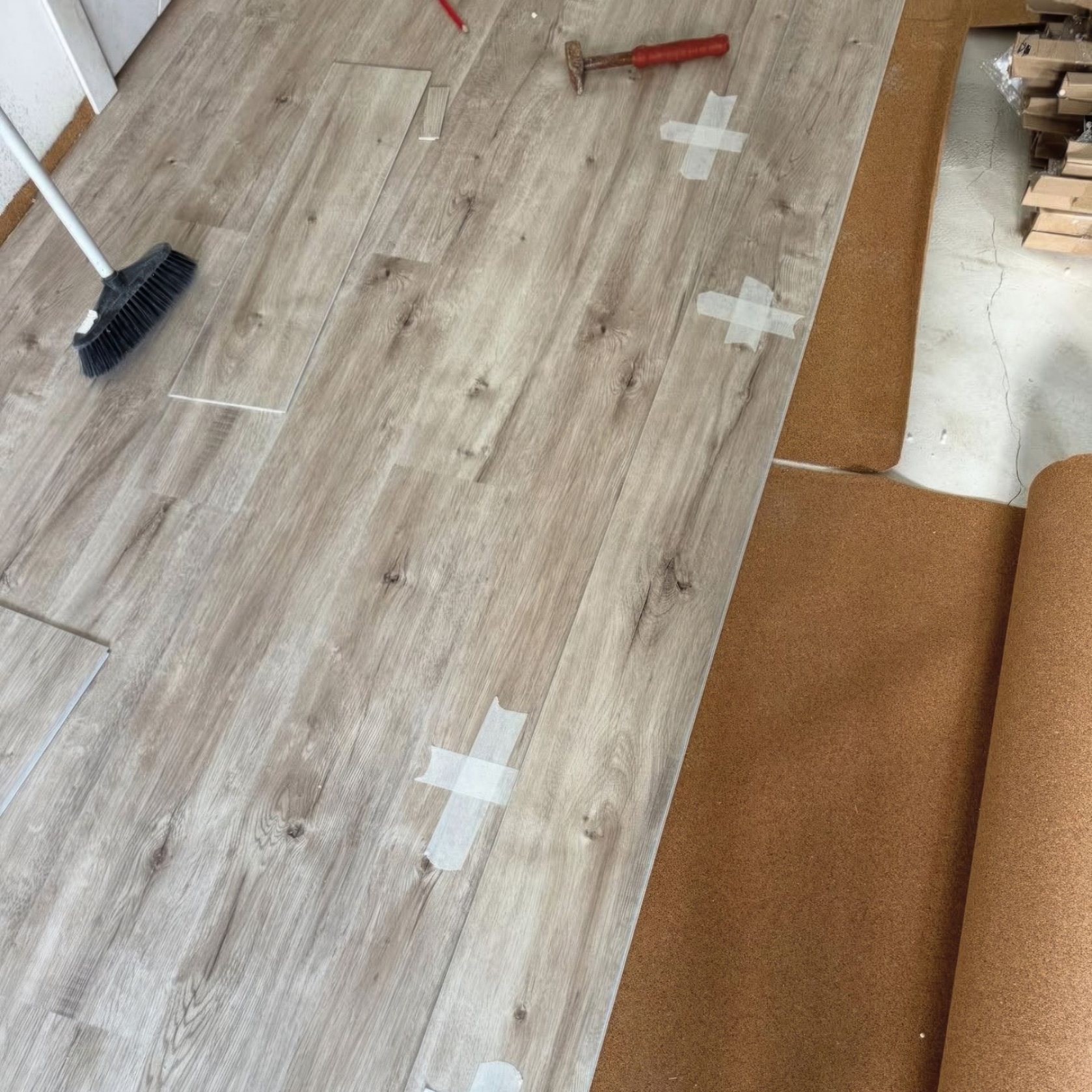 Plancher en bois clair en cours d'installation avec sous-couche en liège ; outils et ruban adhésif visibles.
