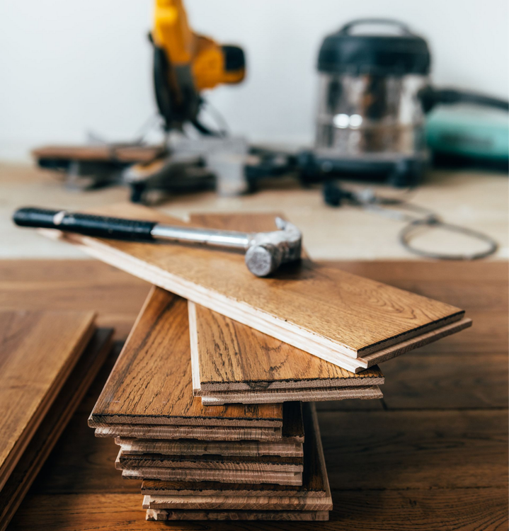 Marteau et planches de bois pour l'installation d'un plancher de bois franc, avec des outils en arrière-plan.
