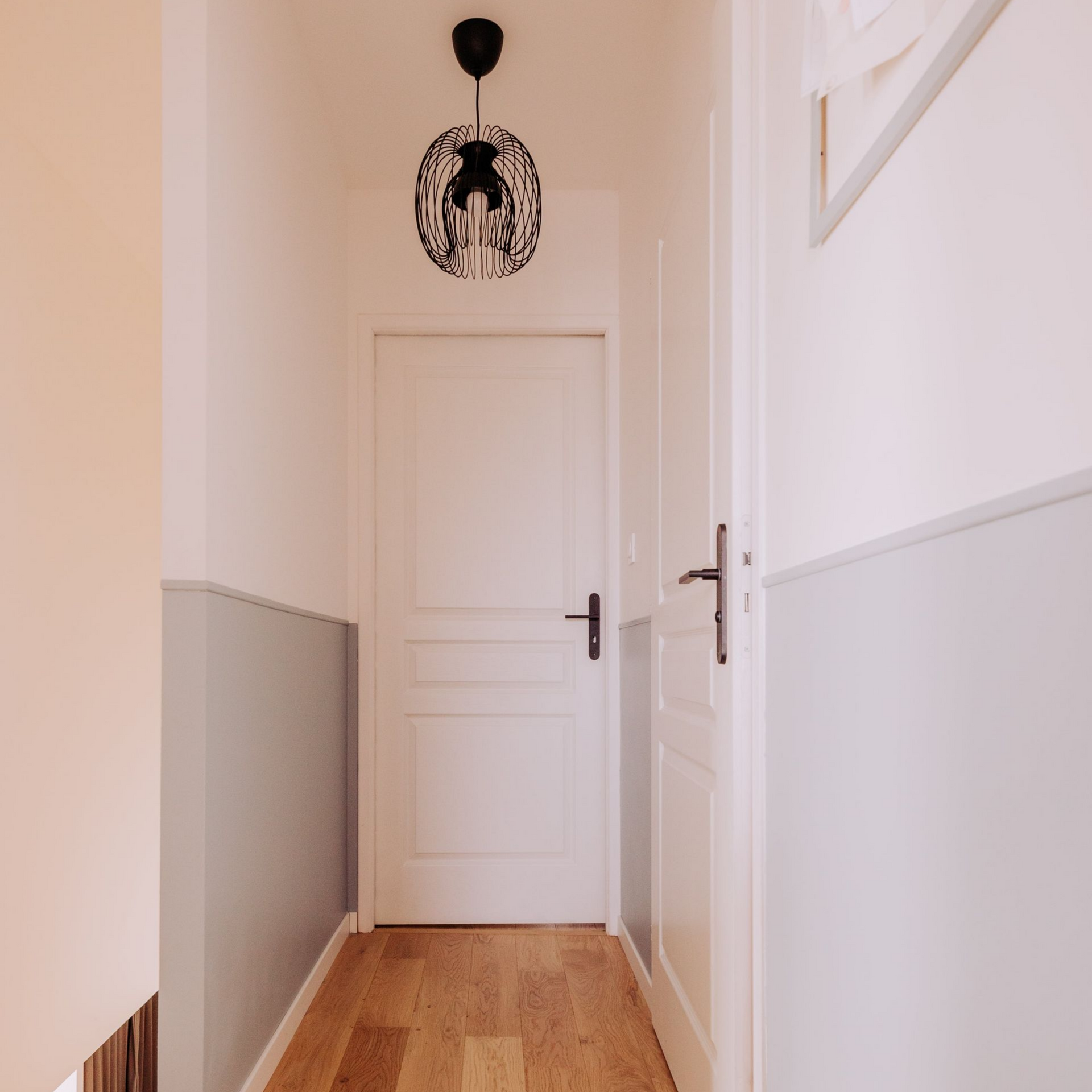 Couloir étroit avec parquet en bois clair, murs blancs et une porte blanche fermée au bout.