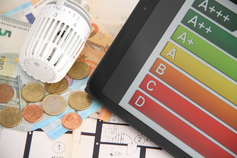Auf einem Tisch liegen ein Thermostat, Münzen und ein Tablet.