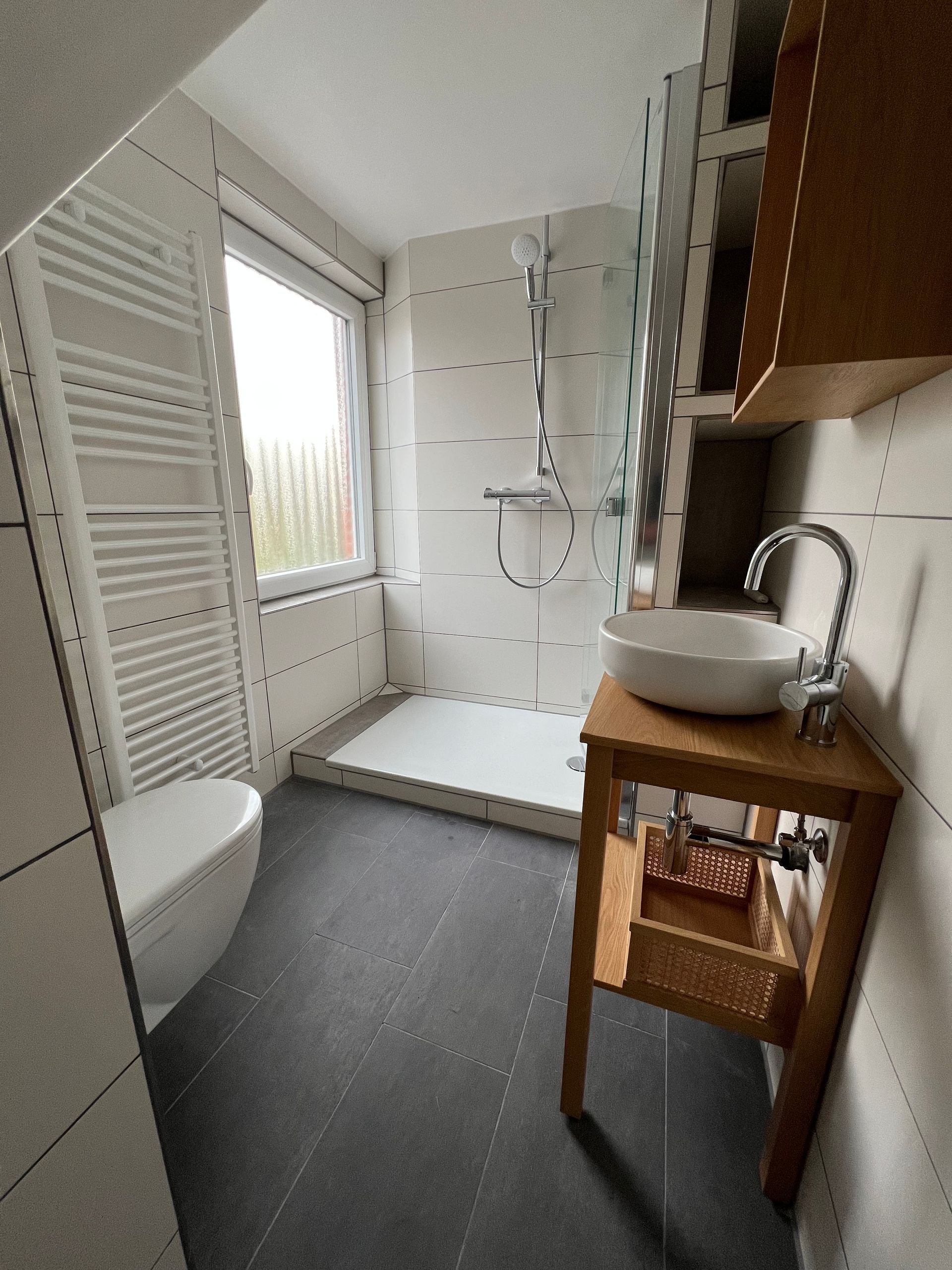 Ein Badezimmer mit Dusche, Waschbecken, WC , in einem kleinen verwinkeltem Bad