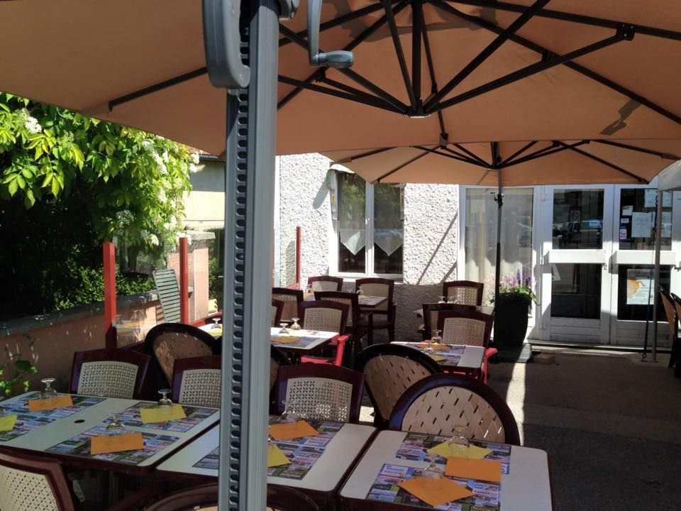 Terrasse de restaurant avec tables, chaises et grand parasol.