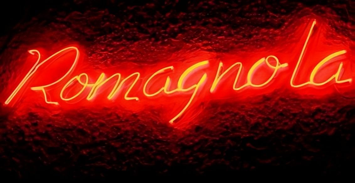 Enseigne lumineuse rouge au néon affichant « Romagnola » sur fond sombre.