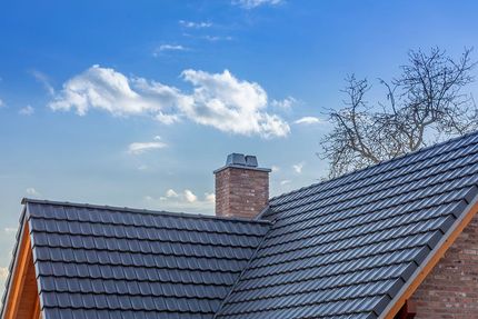 Ein Dach mit einem Schornstein darauf und einem blauen Himmel im Hintergrund.